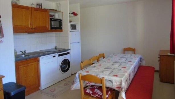 Une cuisine compacte dotée de meubles en bois, d’un four à micro-ondes, d’un lave-linge et d’un coin repas avec une table et des chaises.