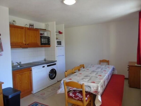A compact kitchen with wooden cabinets, a microwave, a washing machine, and a dining area with a table and chairs.