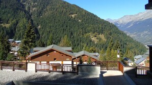 Un chalet de montagne avec des cabanes en bois, une allée de gravier et une vue sur des montagnes boisées.