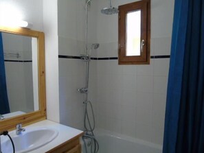 Een badkamer met een witte wastafel, een spiegel, een douche met een handdouche en een raam boven de douche.