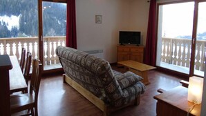A living room with a sofa, wooden furniture, a TV, and large windows with a view of trees and mountains. - 2nd floor, view valley, balcony, tv, ski locker, 61m², Valfréjus (Valfréjus)