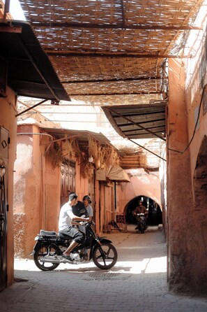A narrow alleyway with a motorcycle parked at the entrance, a person standing beside it, and another person walking away.