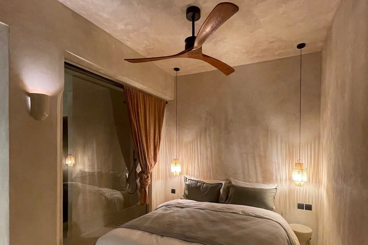 A bedroom with a bed, a ceiling fan, and wall-mounted lights.