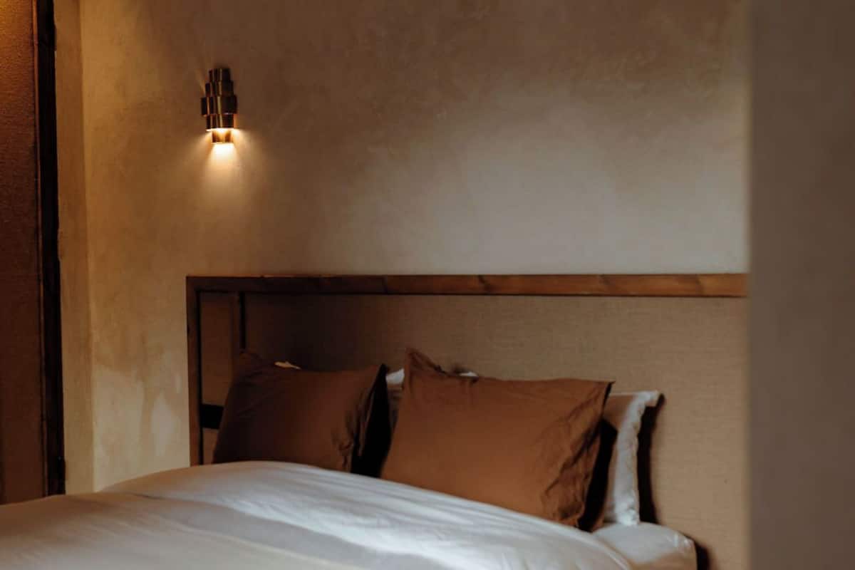 A bedroom with a large bed, a headboard, and a wall-mounted light fixture.