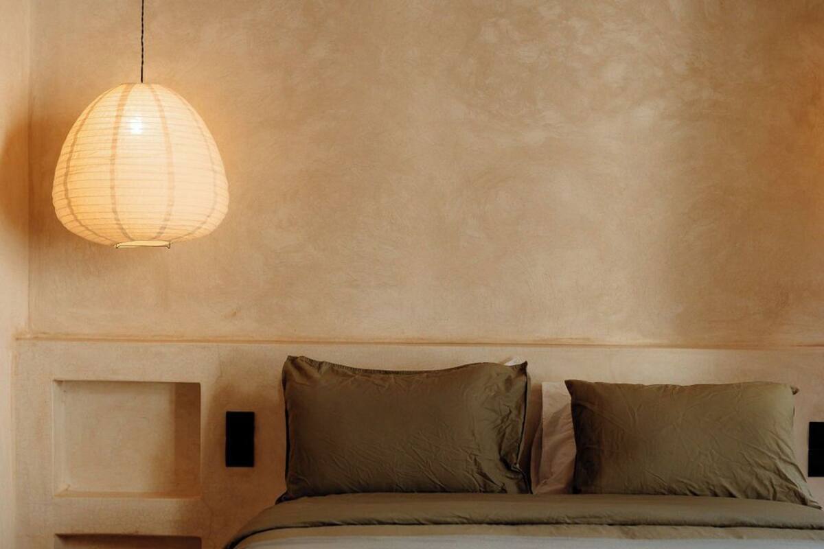 A bedroom with a bed, a hanging light fixture, and a textured wall.