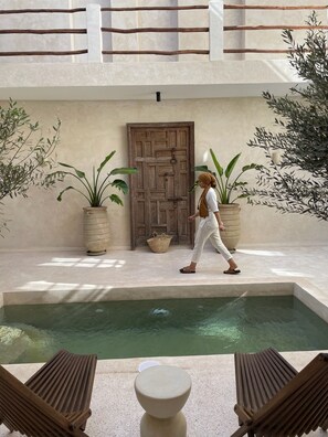 A pool area with a wooden door, potted plants, and lounge chairs. - Riad Roca (Marrakech)