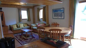 A cozy living room with a sofa, coffee table, and dining table with chairs. There is a window with curtains, a framed picture on the wall, and a trash bin. - 8th floor, view resort, balcony, tv, ski locker, 76m², Valfréjus (Valfréjus)
