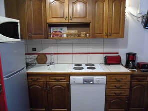A compact kitchen with wooden cabinets, a white stove, a dishwasher, and a red toaster.