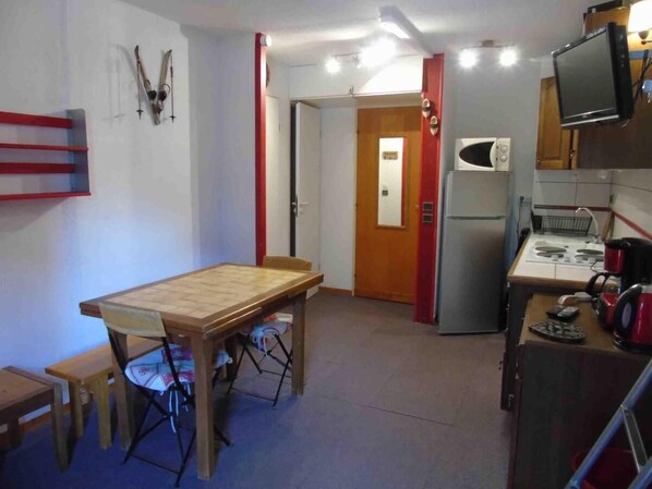 Une cuisine compacte comprenant une table à manger, des chaises, un four à micro-ondes, un réfrigérateur et un téléviseur fixé au mur.