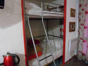 Une chambre avec un lit superposé, une échelle, une bouilloire rouge et un radiateur.