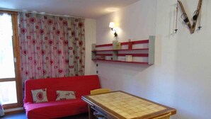 A room with a red sofa, a wooden table with a woven chair, and a wall-mounted shelf with a lamp.