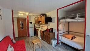 A compact room with bunk beds, a kitchenette, a small dining table, and a red sofa.