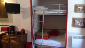 A bunk bed room with a desk, a flat-screen TV, and a coffee maker.