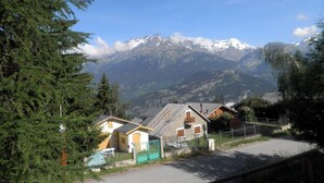 A mountain village with traditional houses, a paved road, and a clear view of snow-capped mountains.