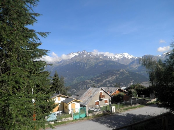 A mountain village with traditional houses, a paved road, and a clear view of snow-capped mountains.