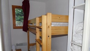 A bunk bed room with a window, a heater, and a small wooden table.