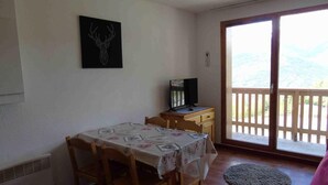A dining area with a table and chairs, a television on a wooden cabinet, and a view through a glass door. - 4th floor, view valley, balcony, tv, ski locker, 26m², Valfréjus (Valfréjus)