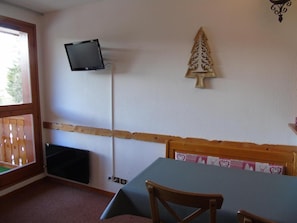 Quarto com uma mesa, cadeiras, televisão na parede e cabeceira de madeira.