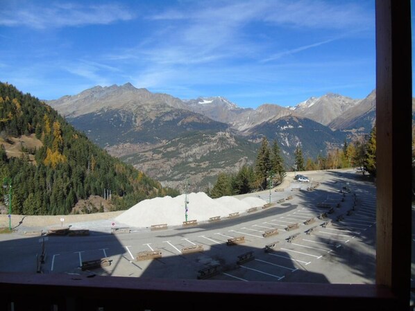 A parking lot with a view of mountains, a pile of gravel, and a few cars.