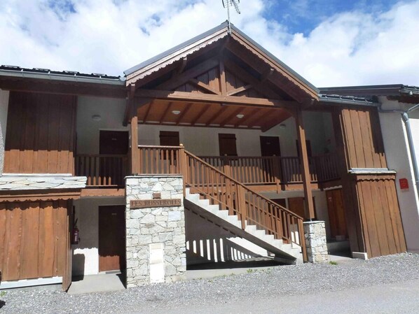 A two-story building with a stone base and wooden upper structure, featuring a staircase with wooden railings and a balcony.