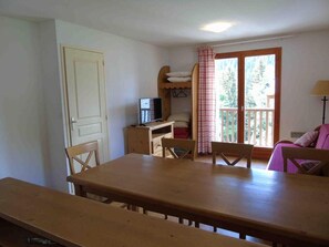 A room with a wooden table and chairs, a TV on a wooden cabinet, a balcony with a checkered curtain, and a lamp. - Ground floor, view mountain, balcony, tv, ski locker, 47m², Valfréjus (Valfréjus)