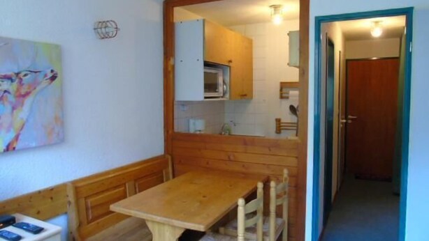Um quarto pequeno e acolhedor, com uma mesa de madeira e um banco, micro-ondas e uma porta que dá para outro cômodo.