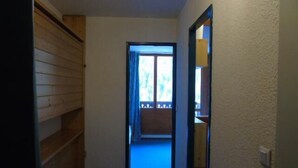 Um corredor estreito com uma estante de madeira à esquerda e uma porta que dá para uma varanda com vista para o exterior.