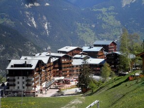 Un chalet de montagne composé de plusieurs bâtiments, doté de balcons, avec une piste de ski en arrière-plan.