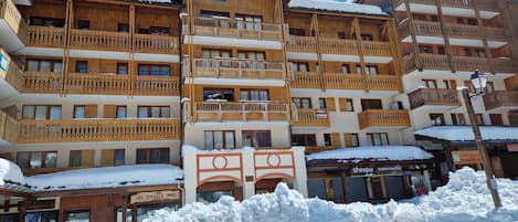 A multi-story wooden building with balconies, a sign for 'Sherpa Supermarché', and snow on the ground.