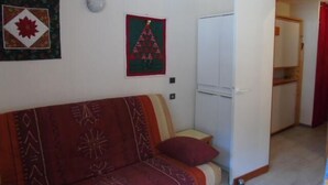 A small, cozy living room with a red sofa, a white wardrobe, and a small table. There are two wall decorations, one with a maple leaf and another with a Christmas tree. - 3rd floor, view valley, balcony, tv, ski locker, 19m², Valfréjus (Valfréjus)