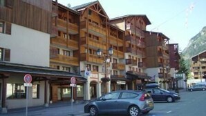 Un hôtel à plusieurs étages doté de balcons, une station de ski en arrière-plan et un ciel dégagé.