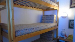 Un lit superposé à trois niveaux, une petite étagère avec des livres et une lampe fixée au mur.