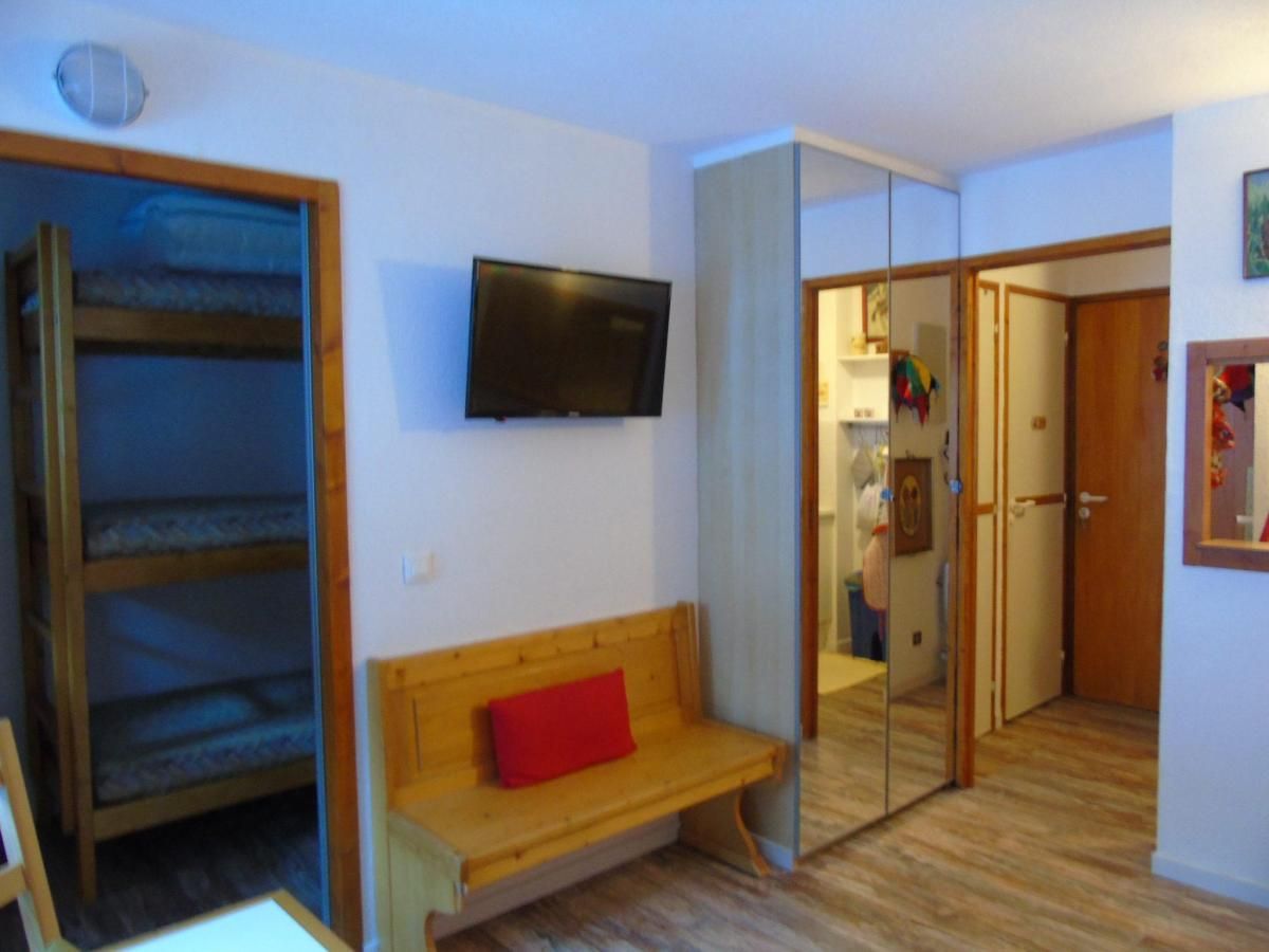 A room with a wooden bench, a television mounted on the wall, and a door leading to another room.