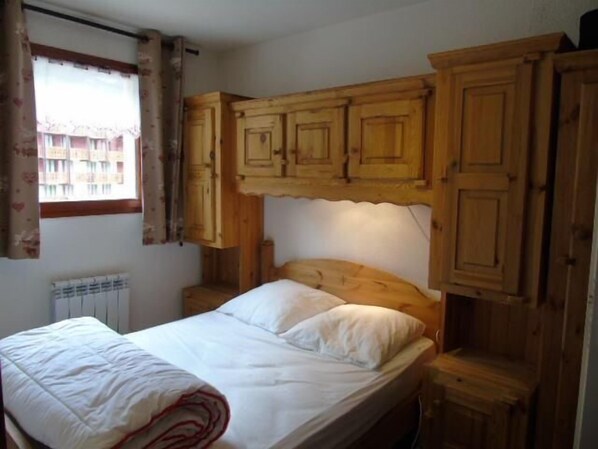 A bedroom with a wooden headboard, a single bed, and built-in wooden cabinets above the bed.