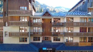 Un hotel de varios pisos con balcones, una señal de esquí y un paisaje montañoso al fondo.