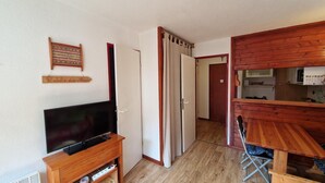 Una habitación compacta con televisión sobre un soporte de madera, una mesa de comedor de madera y una zona de cocina con mostrador de madera.
