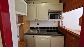 Una cocina compacta con armarios blancos, encimera negra, microondas, lavavajillas y un lavabo.