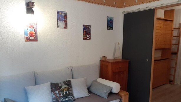 A cozy room with a sofa, pillows, a small wooden side table, and a door leading to another room. - 50m from ski lifts, 2nd floor, balcony, tv, ski locker, 19m², Valfréjus (Valfréjus)