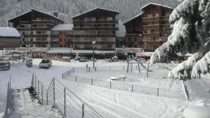 A snow-covered ski resort with wooden buildings, a fenced parking area, and a mountainous backdrop. - 50m from ski lifts, 2nd floor, balcony, tv, ski locker, 19m², Valfréjus (Valfréjus)