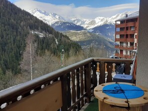Un balcone con vista su montagne innevate, una ringhiera in legno e un tavolino con un sottotavolo blu.
