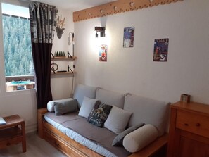 A cozy room with a sofa bed, a small wooden table, and a window with curtains. - 50m from ski lifts, 2nd floor, balcony, tv, ski locker, 19m², Valfréjus (Valfréjus)