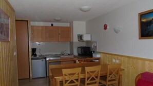 A compact kitchen with wooden cabinets, a microwave, and a coffee maker. There is a dining area with wooden chairs and a table. - Ground floor, view valley, balcony, tv, ski locker, 33m², Valfréjus (Valfréjus)