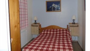 A bedroom with a wooden bed, checkered bedding, two bedside tables with lamps, a wall-mounted painting, and a window with a checkered curtain. - Ground floor, view valley, balcony, tv, ski locker, 33m², Valfréjus (Valfréjus)