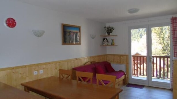 A dining area with a wooden table and chairs, a bench with a red cushion, a painting on the wall, and a sliding glass door leading to an outdoor area. - Ground floor, view valley, balcony, tv, ski locker, 33m², Valfréjus (Valfréjus)