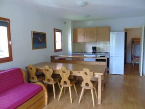 A compact kitchen with wooden cabinets, a dining table with chairs, a refrigerator, and a pink sofa. - 1st floor, view valley, balcony, tv, ski locker, 48m², Valfréjus (Valfréjus)