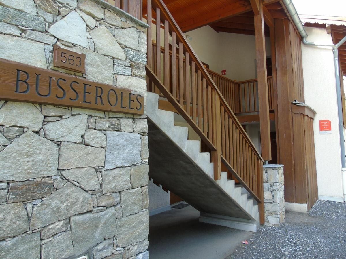 A stone wall with a wooden sign reading "BUSSEROLES" and a wooden staircase leading to a covered entrance.