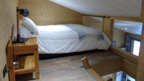 Une petite pièce en bois, avec un lit simple, un bureau et une fenêtre.