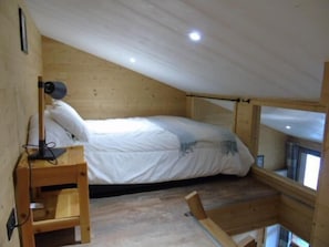 Ein kleines Zimmer mit Holzboden, einem Bett, einem Schreibtisch und einem Fenster.