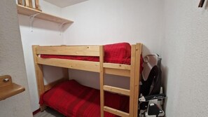 A bunk bed with a red blanket, a wooden shelf above, and a bicycle rack against the wall.