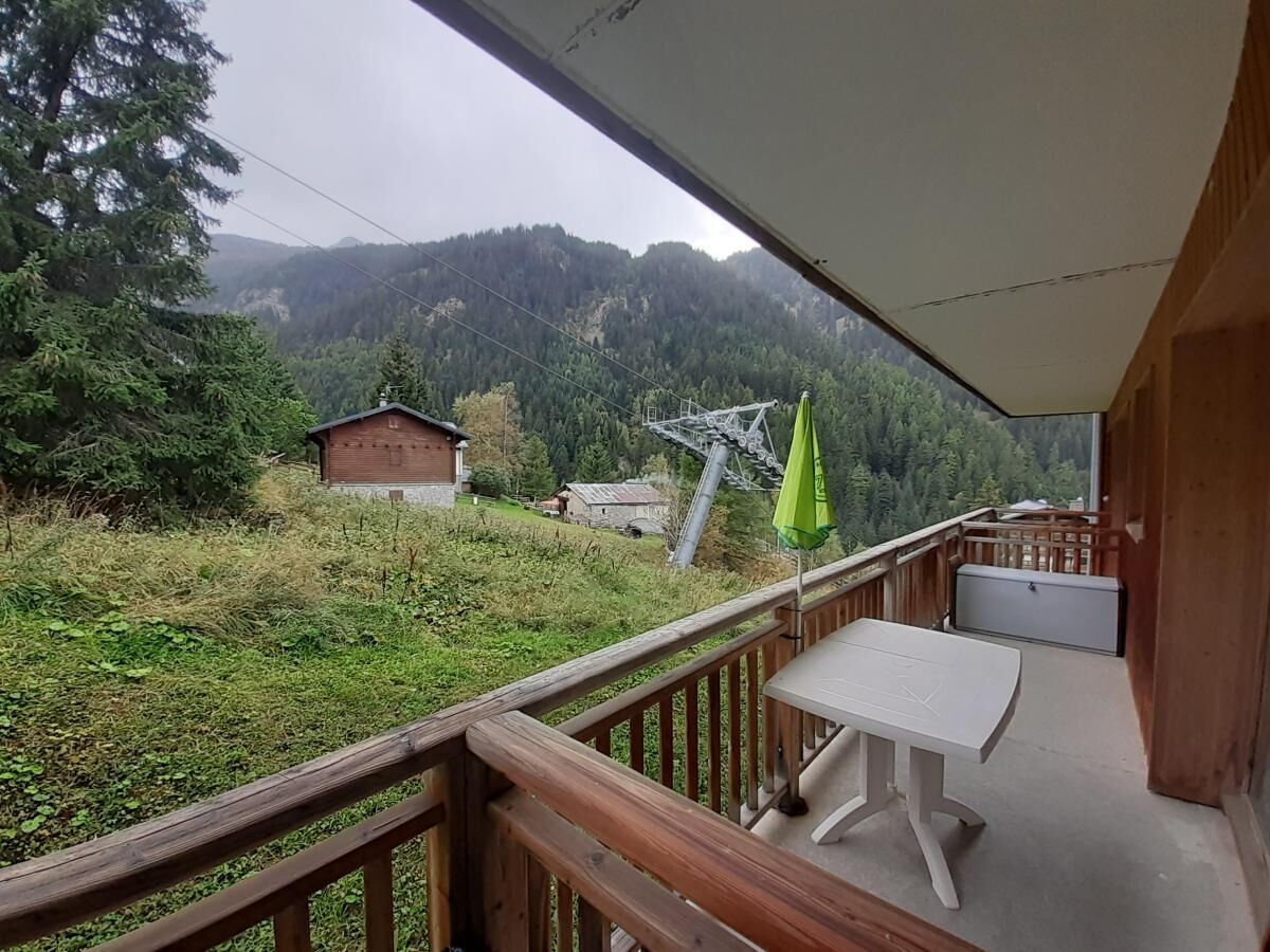 A balcony with a table and a green umbrella, overlooking a forested valley with a mountain in the background.
